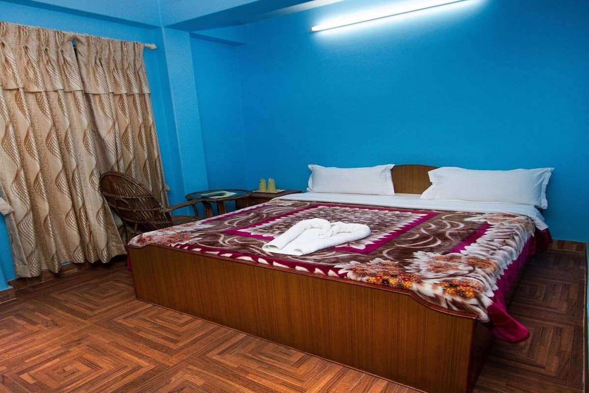 A hotel room with a large bed, a wooden headboard, a small table with a chair, and a curtain.