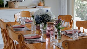 Un coin repas avec une table en bois dressée pour quatre personnes, entourée de chaises en bois. Un miroir est accroché au mur au-dessus de la table, et une fenêtre avec des rideaux se trouve à droite.