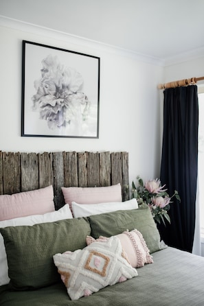A bedroom with a wooden headboard, green and white bedding, and a framed floral artwork on the wall.