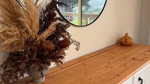 Un meuble en bois surmonté d’un miroir, un vase contenant des plantes séchées et un bol en bois posé sur le meuble.