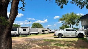 Un camping con vehículos recreativos y una camioneta pickup blanca estacionada sobre un camino de tierra.