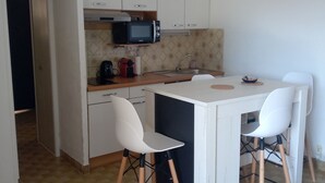 A compact kitchen with white cabinets, a microwave, a sink, and two white chairs. - Comfortable apartment with large terrace and lake view (Sainte-Croix-du-Verdon)