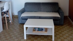 A living room with a grey sofa, a white coffee table, a dining table with chairs, and a hanging light fixture. - Comfortable apartment with large terrace and lake view (Sainte-Croix-du-Verdon)