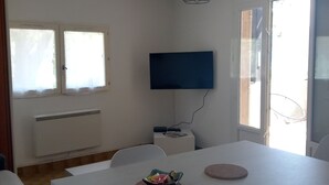 A room with a white table, chairs, a flat-screen TV mounted on the wall, a ceiling light fixture, and a window with a view outside. - Comfortable apartment with large terrace and lake view (Sainte-Croix-du-Verdon)