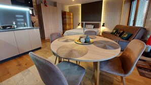 Un salon moderne avec une table ronde en bois, des fauteuils à revêtement gris, un canapé et un coin cuisine équipé d’un four à micro-ondes.