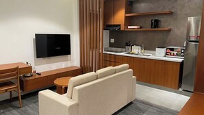 Een moderne woonkamer met een bank, een televisie, een eettafel en een keuken met een koelkast, magnetron en fornuis.