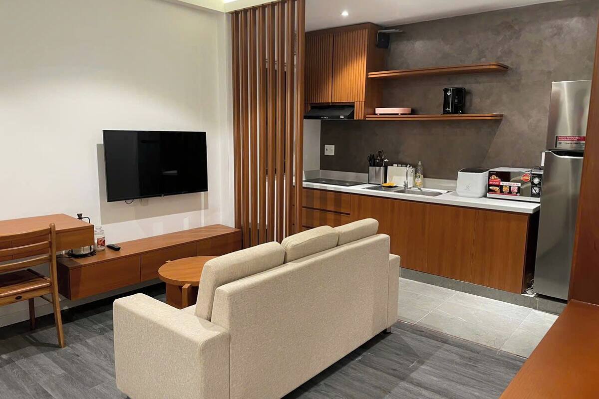 A modern living room with a sofa, a TV, a dining table, and a kitchen area with a refrigerator, microwave, and stove.