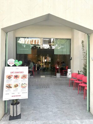 L’entrée d’un restaurant, avec un panneau affichant le menu intitulé « LES SPÉCIALITÉS DE LIM », où sont présentés différents plats.