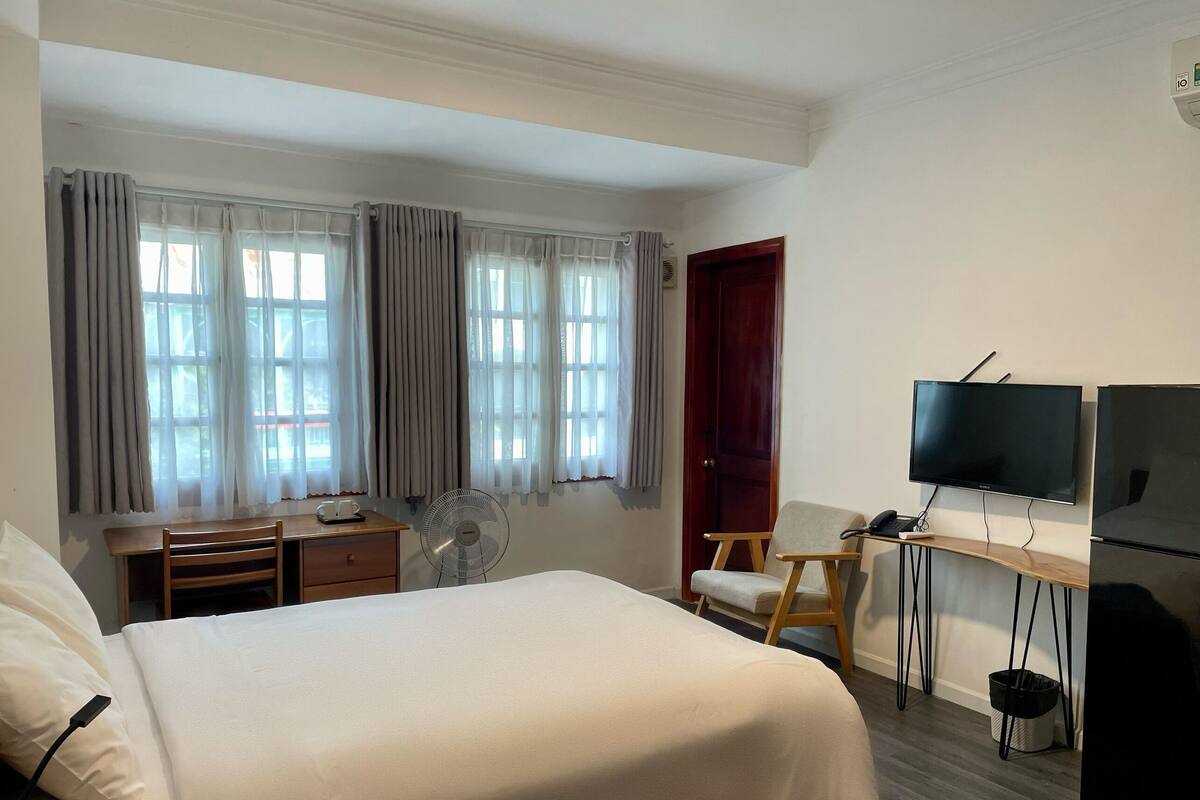 A hotel room with a bed, a desk with a chair, a television, and a window with curtains.