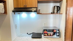 Een kleine keuken met houten kastjes, een ingebouwde magnetron en een waterkoker.