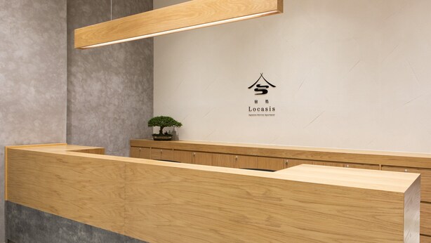 Een receptiebalie met een houten afwerking, een potplant en een bord met het Locasis logo.