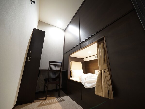 A compact room with a bed, a chair, and a window with curtains.