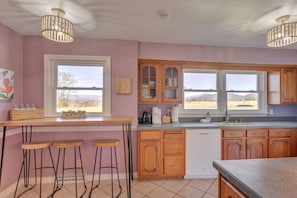 Une cuisine avec des meubles en bois, un coin bar avec des tabourets et une vue sur l’extérieur.