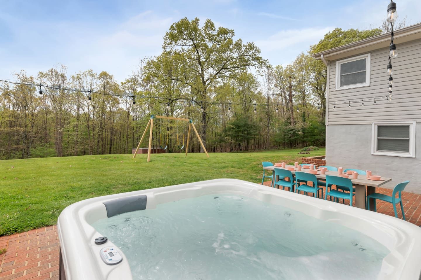 Un patio trasero con un jacuzzi, un columpio y una zona de estar con sillas y una mesa.