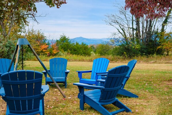Un espacio exterior cubierto de césped, con varias sillas Adirondack azules y un conjunto de columpios.