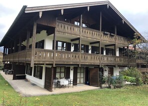 Traditional chalet-style building with a central entrance and multiple balconies, set amidst a serene lawn and trees.