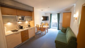 A compact kitchen with a microwave, stove, and sink. There is a dining area with a table and chairs, and a green sofa in the living area.
