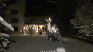 Un edificio cubierto de nieve con una entrada iluminada y una valla de madera en primer plano.