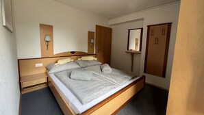 Un dormitorio con una cama de madera, una mesita de noche, una lámpara de pared, un espejo y un armario.
