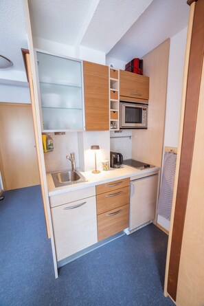 Pieni, käytännöllinen keittiö, jossa on mikroaaltouuni, pesuallas ja säilytystilaa tarjoavat kaapit.
