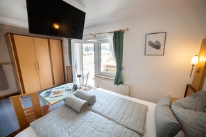 A hotel room with a bed, a desk, a wardrobe, a TV, a window with curtains, and a painting on the wall. - Almstudio [3] - Apartments Hohenberger (Mallnitz)