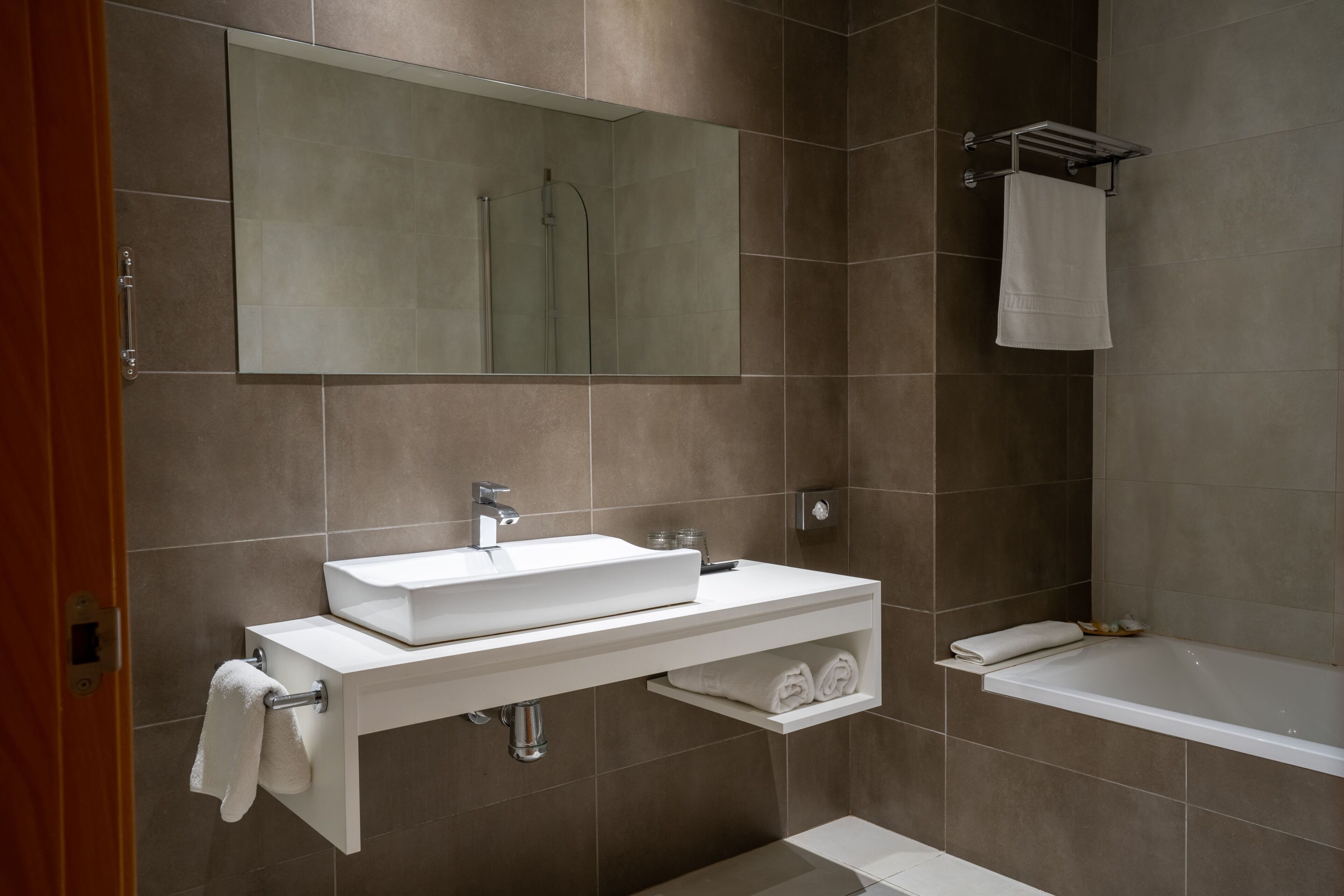 Ein modernes Badezimmer mit großem Spiegel, Waschbecken, Badewanne und Handtuchhalter.