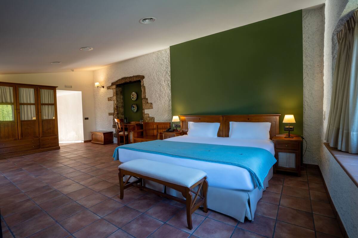 A bedroom with a large bed, a bench, a wooden wardrobe, and a green wall.