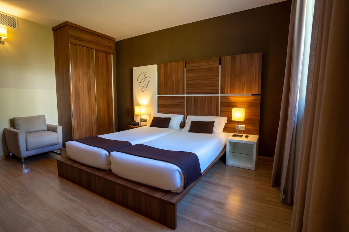 A modern hotel room with a large bed, a sofa, a nightstand, and a wall-mounted TV.