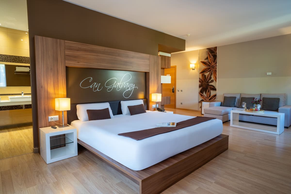A modern hotel room with a large bed, bedside tables, a sofa, and a wall-mounted TV.