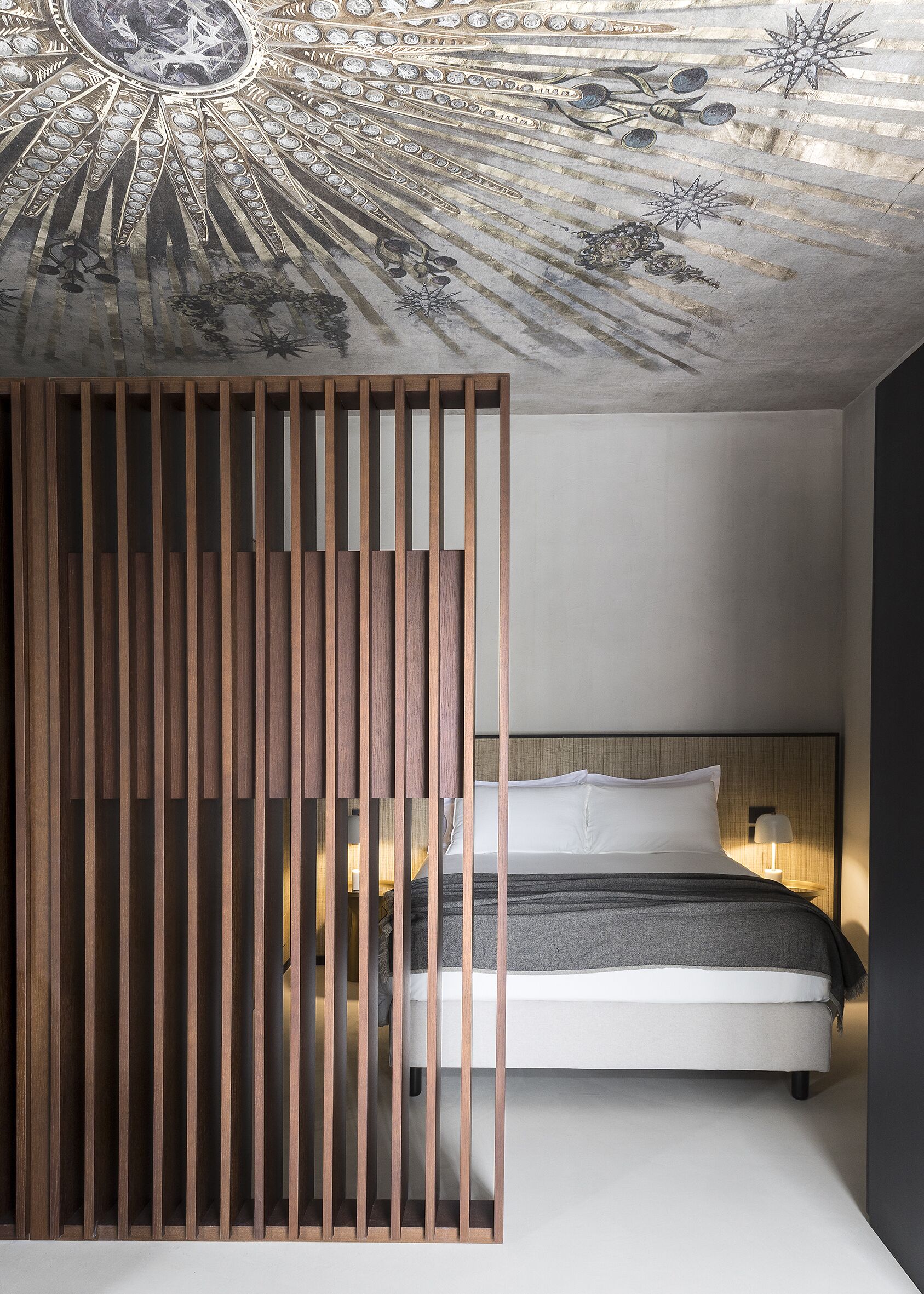 A bedroom with a bed, a wooden partition, and a ceiling with a star-like design.