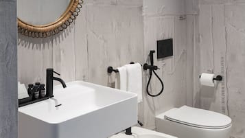 A modern bathroom with a white sink, a round mirror with a wooden frame, a bidet, and a toilet.