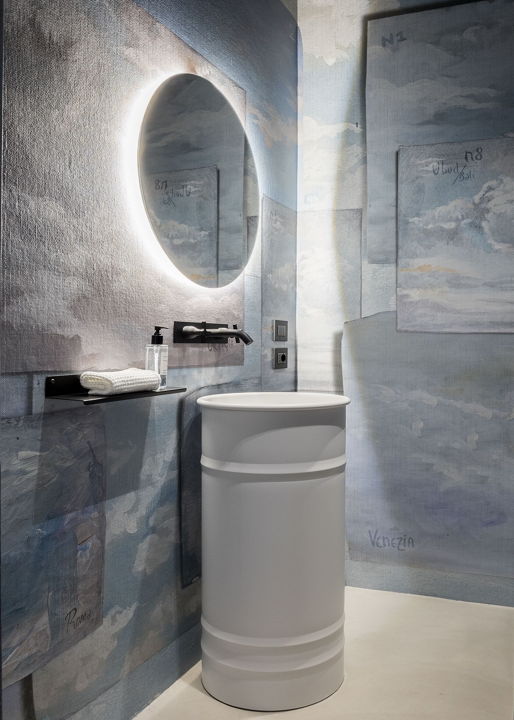 A modern bathroom with a large round mirror, a white sink, and a textured wall.