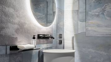 A modern bathroom with a large round mirror, a white sink, and a textured wall.