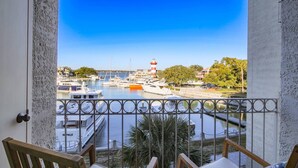 Un balcón con vistas a un puerto deportivo, que incluye barcos y un faro.