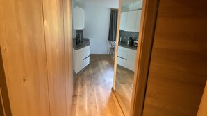 A narrow hallway with wooden flooring leading to a kitchen area with white cabinets and a countertop. - Alpenhome Apartment [6] - Apartments Hohenberger (Mallnitz)