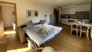 A compact hotel room with a bed, bedside table, and a kitchenette. - Alpenhome Apartment [6] - Apartments Hohenberger (Mallnitz)