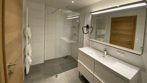 A modern bathroom with a glass-enclosed shower, a vanity with a mirror, and a towel rack. - Alpenhome Apartment [6] - Apartments Hohenberger (Mallnitz)