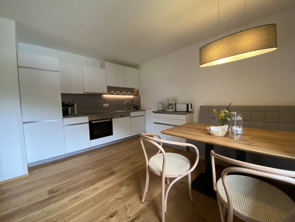 Une cuisine moderne avec des meubles blancs, une table à manger en bois et deux chaises en osier.