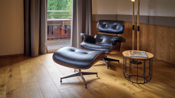 Ein modernes Zimmer mit einem Ledersessel, einem kleinen runden Tisch mit einer Zeitschrift und einer stehenden Stehlampe.