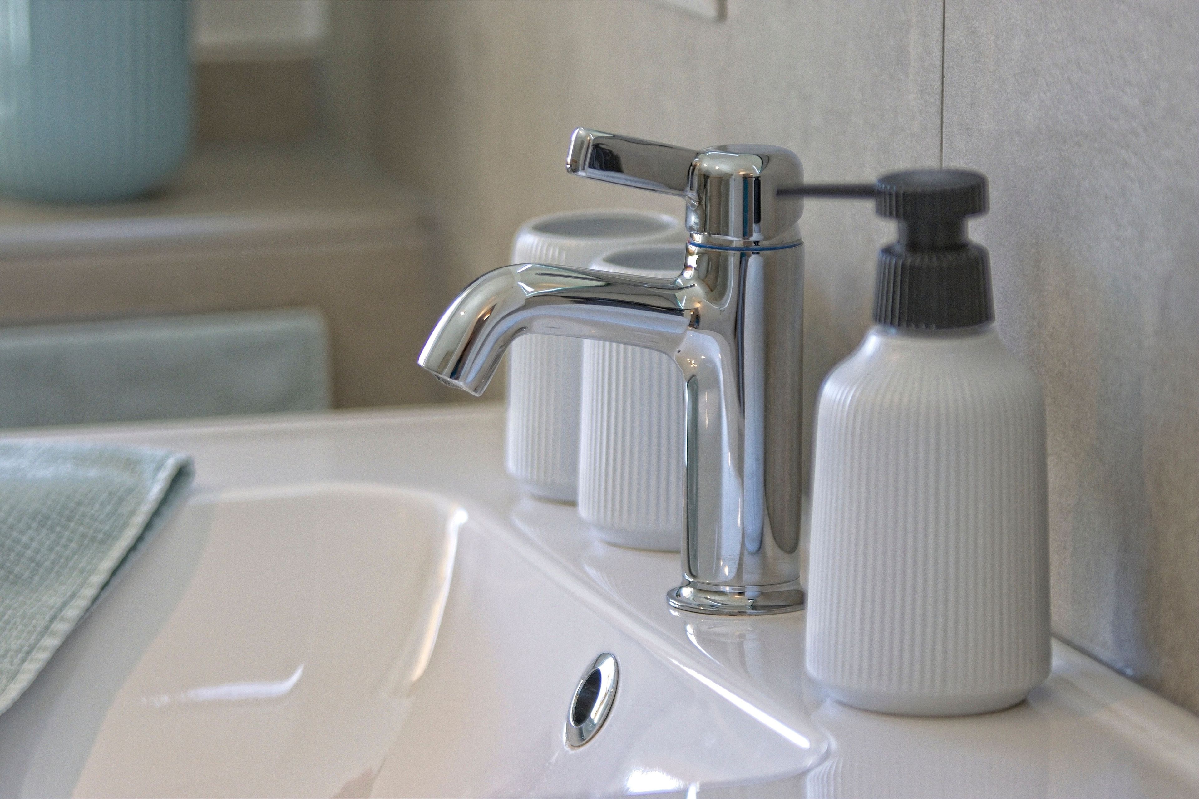 A bathroom sink with a chrome faucet, a soap dispenser, and a towel.