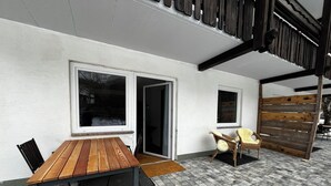 An outdoor patio area with a wooden table and chairs, a sliding glass door, and a wooden fence.