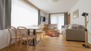 Una sala de estar moderna con una mesa de comedor de madera, sillas, un sofá y un televisor montado en la pared.