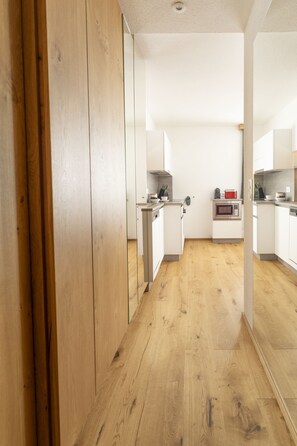A narrow hallway with wooden flooring leading to a kitchen area with white cabinets and a microwave. - Alpenhome Apartment [I] - Apartments Hohenberger (Mallnitz)