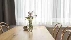 Un comedor con una mesa de madera, cuatro sillas de mimbre, un jarrón con flores y cortinas de encaje.