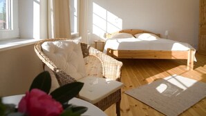 Une chambre à coucher avec un lit en bois, une chaise en osier, une table de chevet et une fenêtre avec des rideaux.