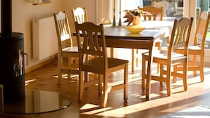 Un comedor con mesa y sillas de madera, estufa negra y ventana que proporciona luz natural.