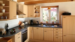 Una cocina con armarios de madera, estufa, lavamanos y ventana con vistas al verdor.