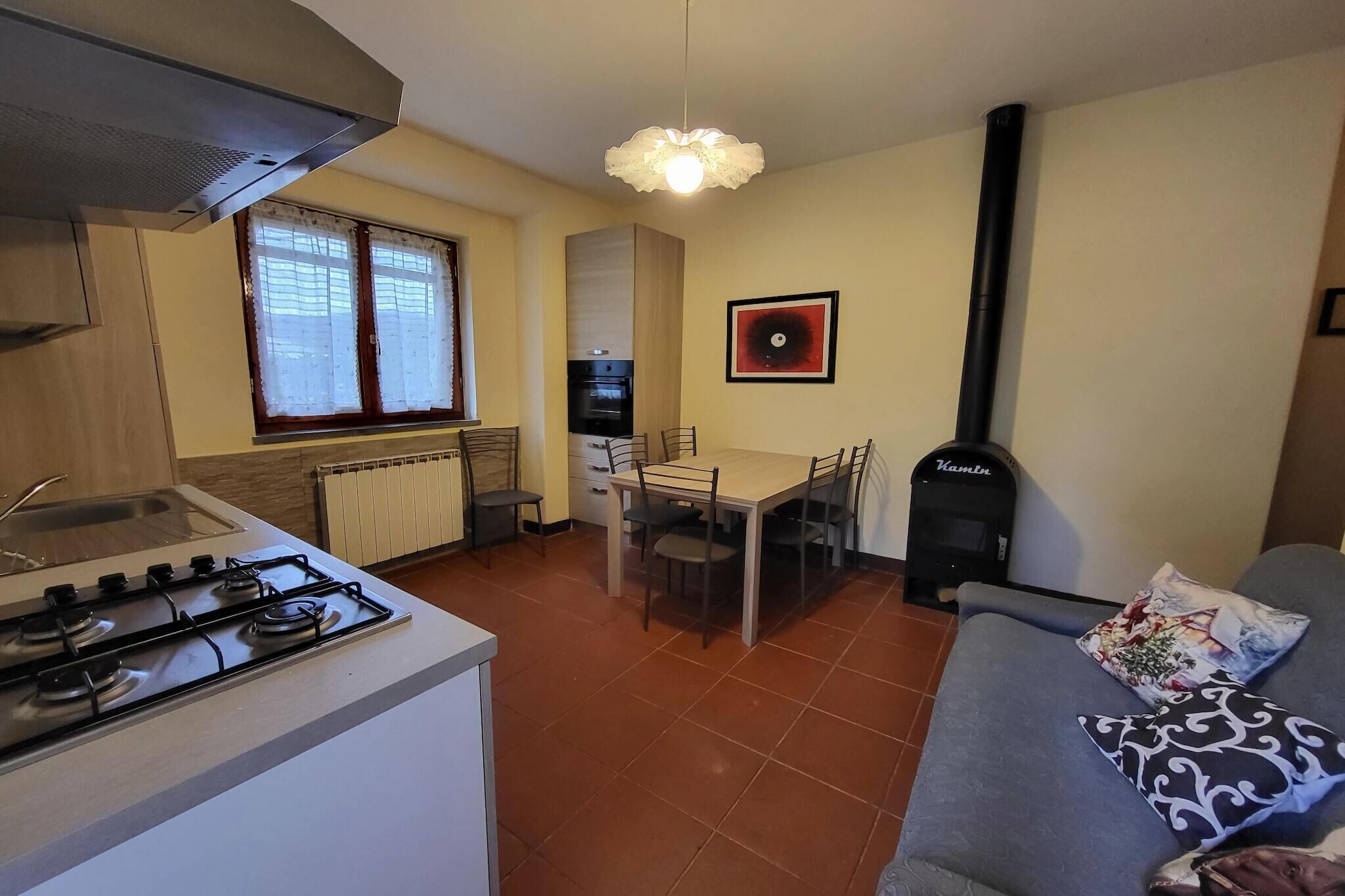 Una cocina compacta con estufa a gas, una mesa de comedor con sillas, horno empotrado y estufa de leña negra.