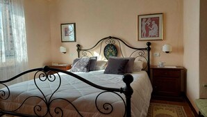 Un dormitorio con cama, mesita de noche, lámpara, cuadro enmarco y ventana con cortinas.