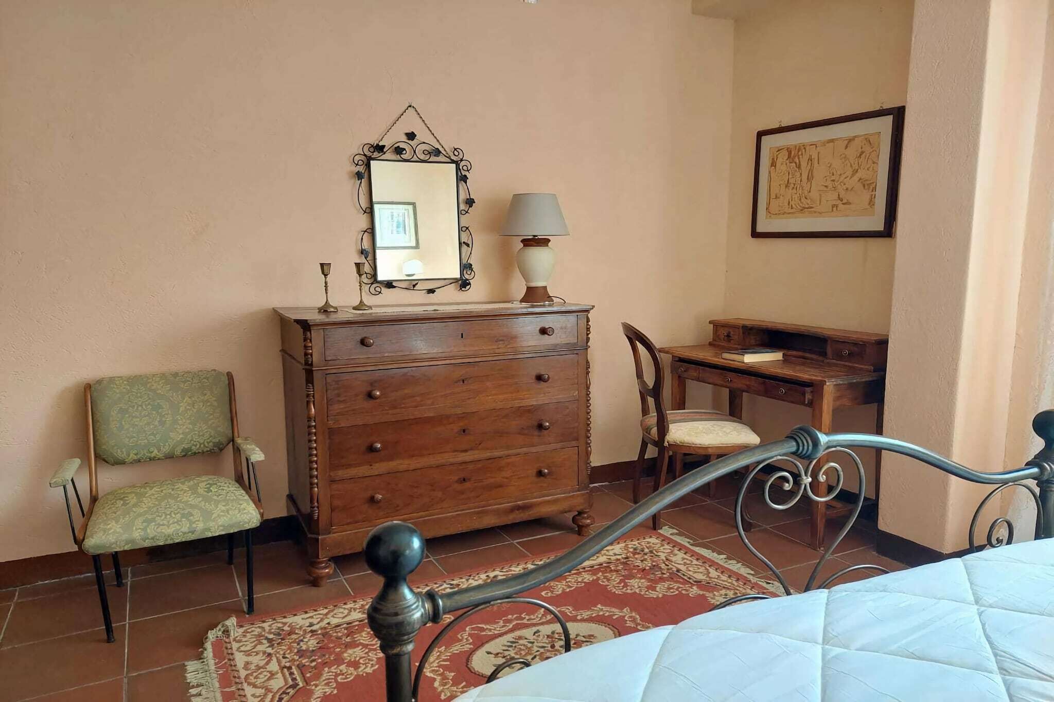 A bedroom with a bed, a wooden dresser, a chair, a desk, a mirror, and a lamp.